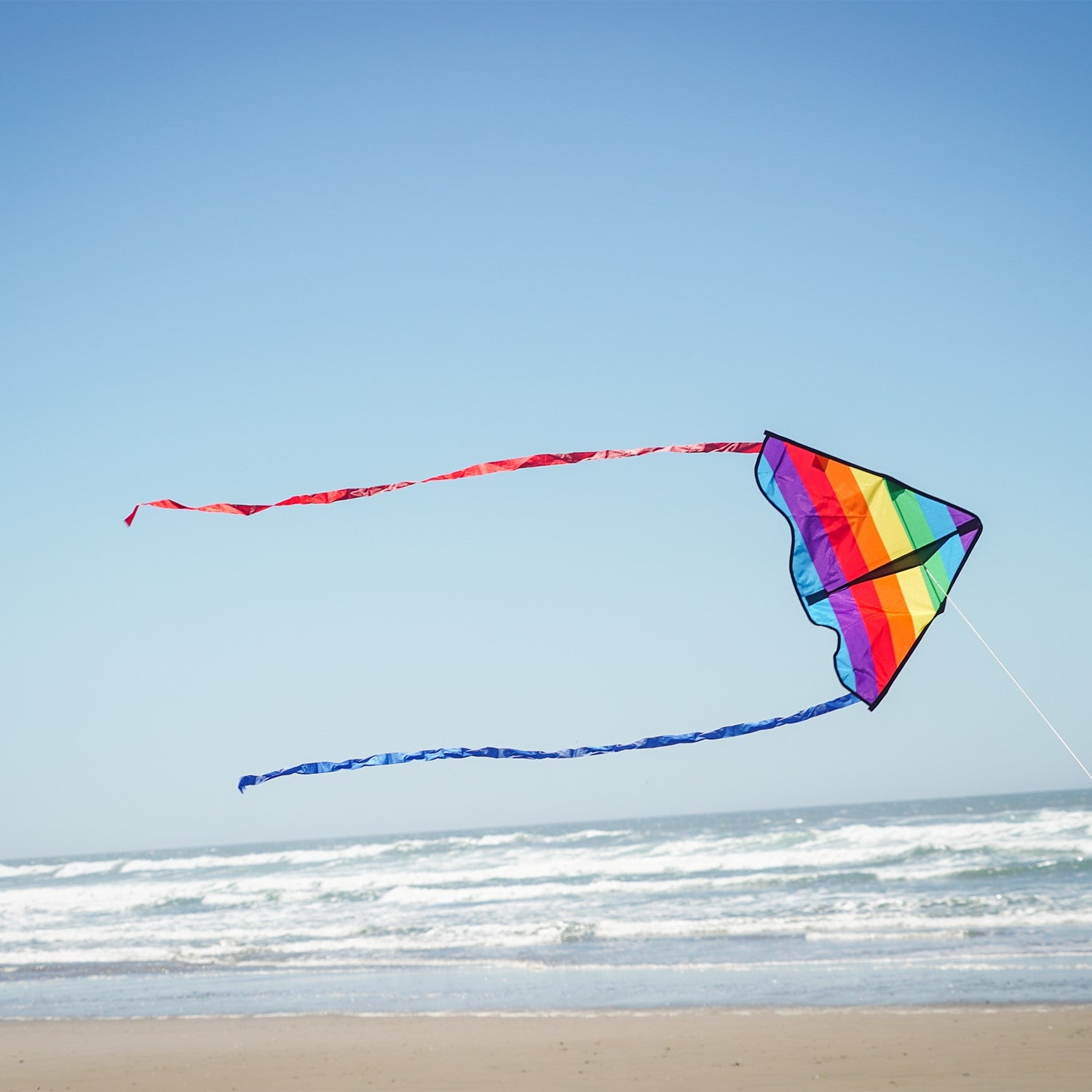 Colorful Rainbow Stripe 30-inch Delta Kite, featuring durable ripstop fabric and stable design, displayed soaring in a bright blue sky with playful tails fluttering below.