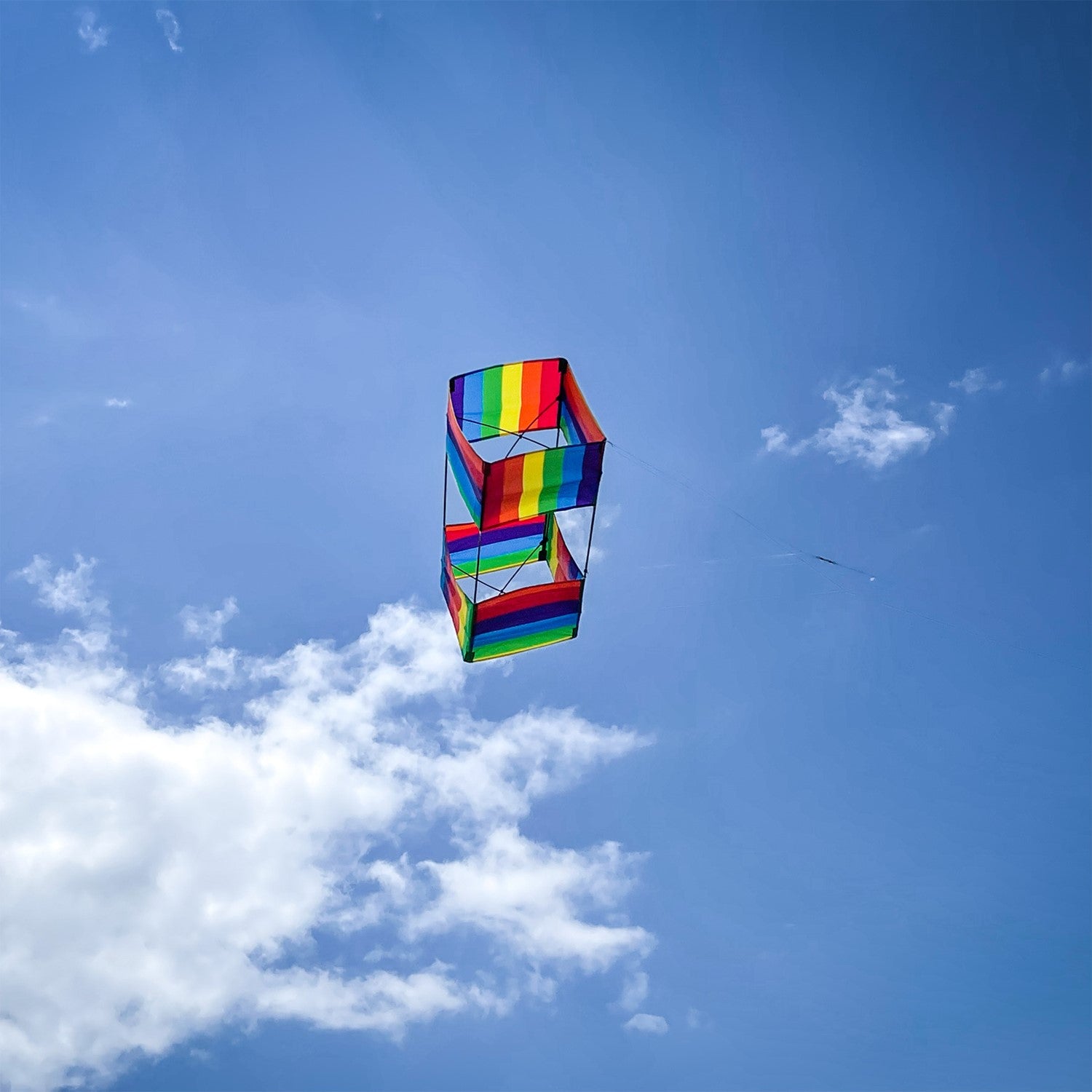 Rainbow Stripe Box Kite in mid-flight with colorful stripes against a clear blue sky, showcasing its vibrant 3D design.
