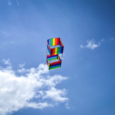 Rainbow Stripe Box Kite in mid-flight with colorful stripes against a clear blue sky, showcasing its vibrant 3D design.