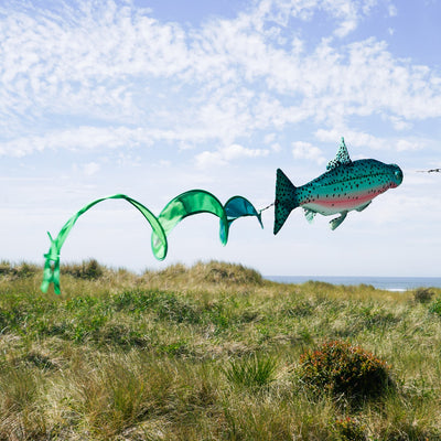 Rainbow Trout Spinner Tail wind sock with vibrant colors and spinning streamer tail, hanging outdoors in a garden setting.
