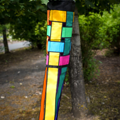 Colorful Rainbow Weave 40" Windsock with black edging and fluttering tails displayed outdoors, showcasing vivid colors against the backdrop.