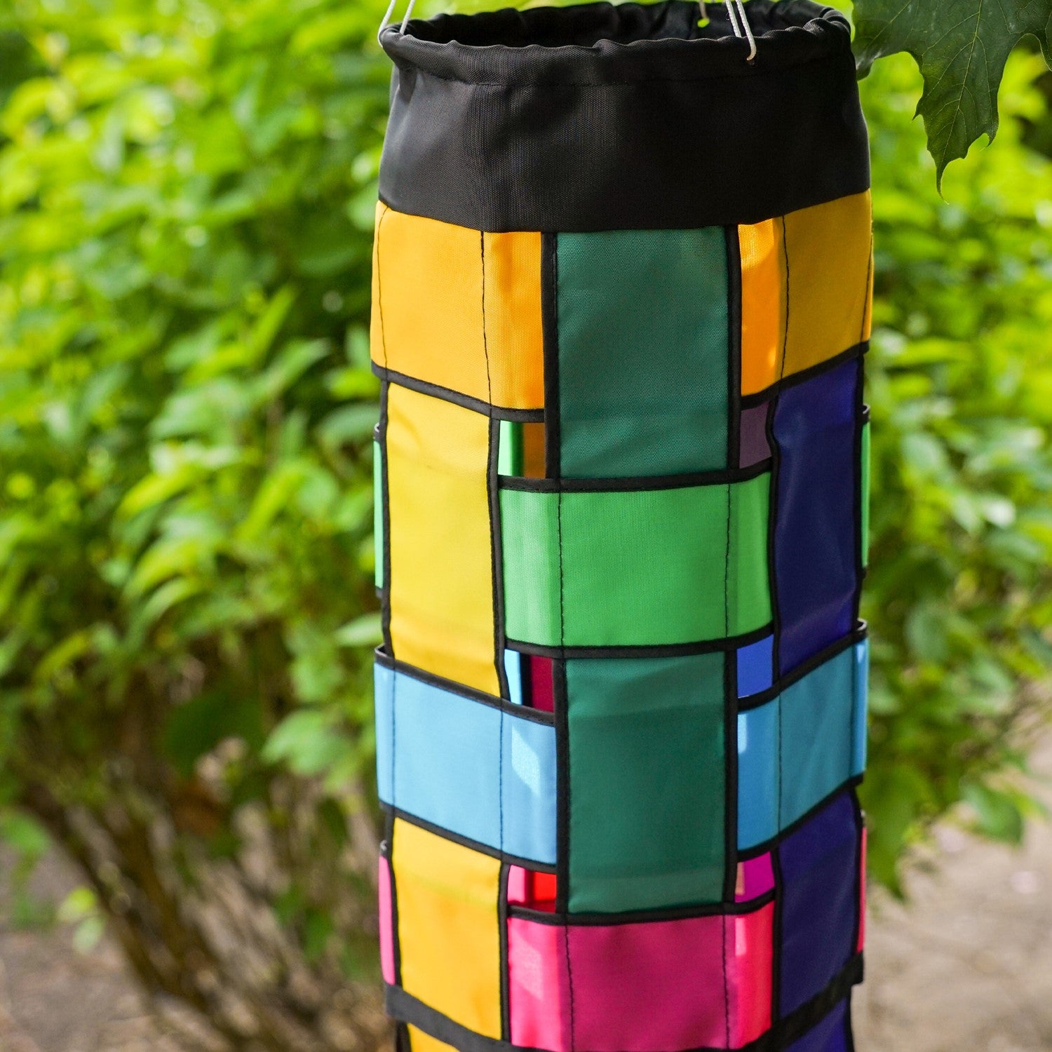 Colorful Rainbow Weave 40" Windsock with black edging and fluttering tails displayed outdoors, showcasing vivid colors against the backdrop.