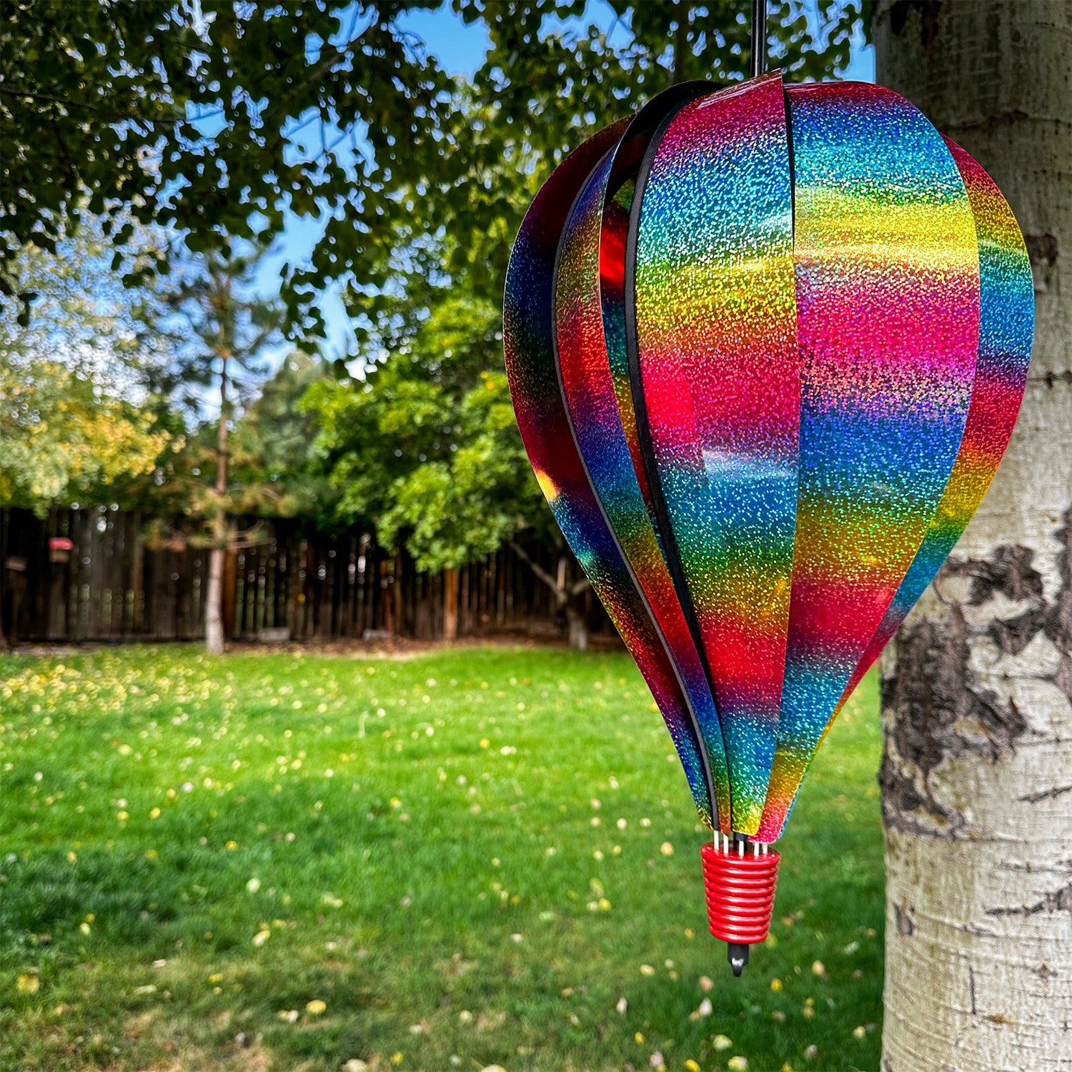Rainbow Whirl 10-Panel Hot Air Balloon spinner with a sparkling Mylar design, displaying vibrant colors in a garden setting.