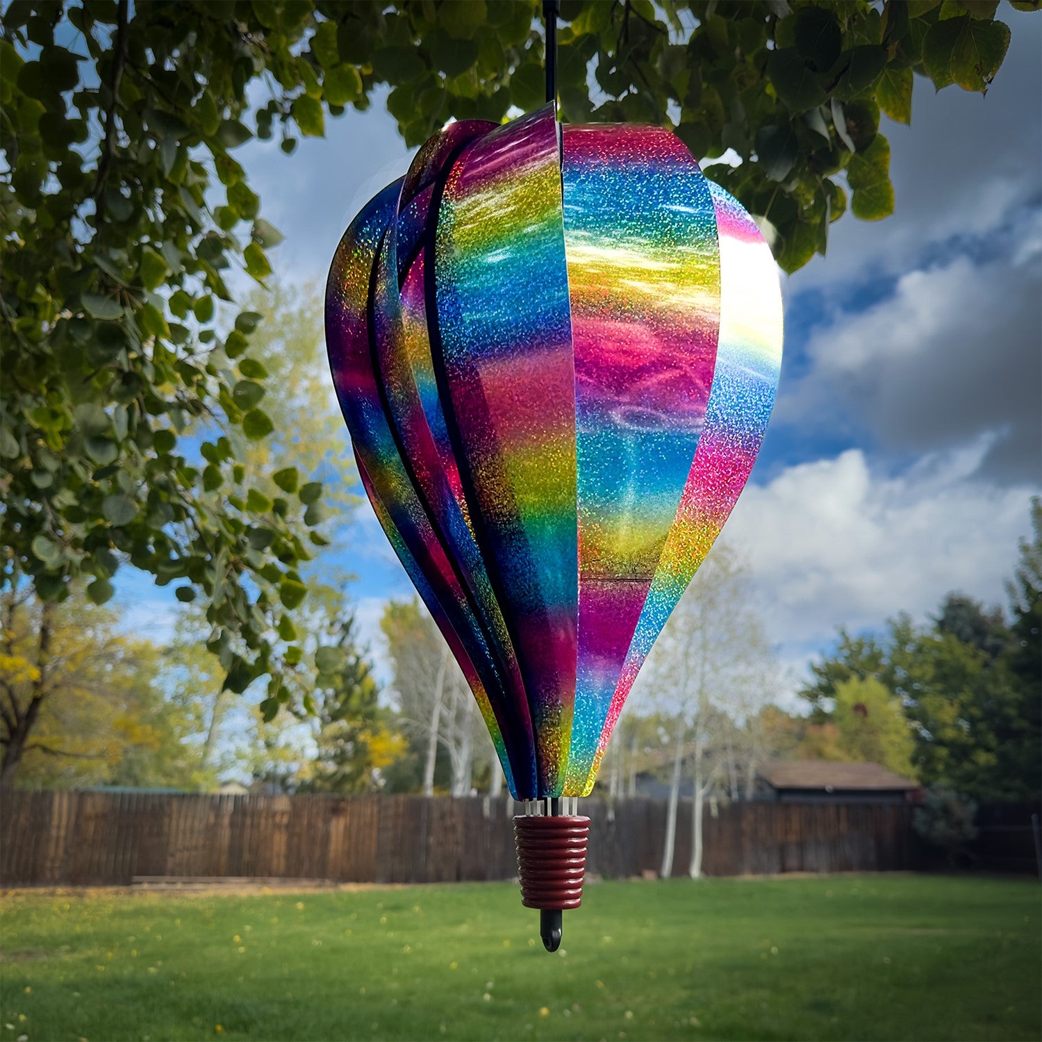 Rainbow Whirl 10-Panel Hot Air Balloon spinner with a sparkling Mylar design, displaying vibrant colors in a garden setting.