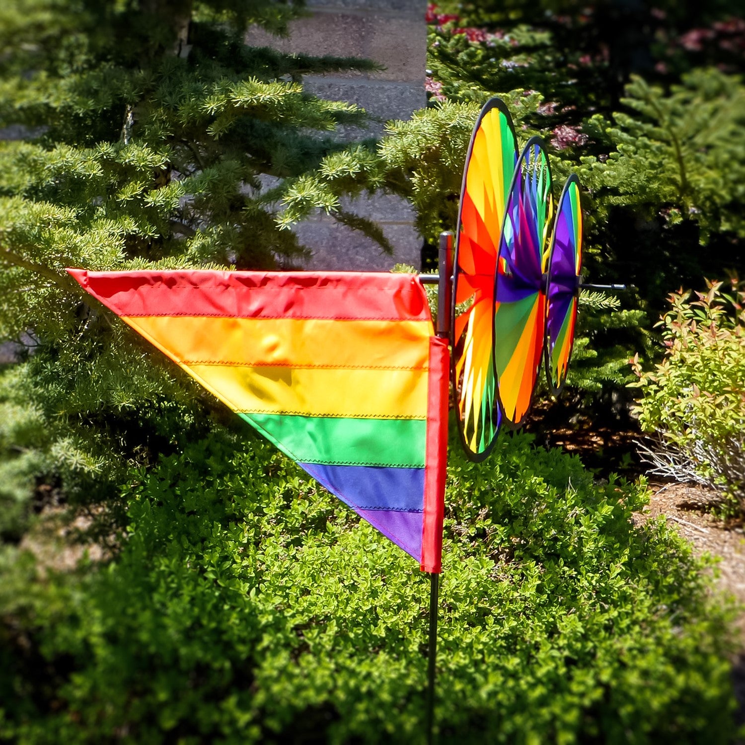 Rainbow Wind Sail Triple Wheel Spinner showcasing three spinning wheels in a rainbow spectrum, set against a clear blue sky with a pivoting pole for wind display.