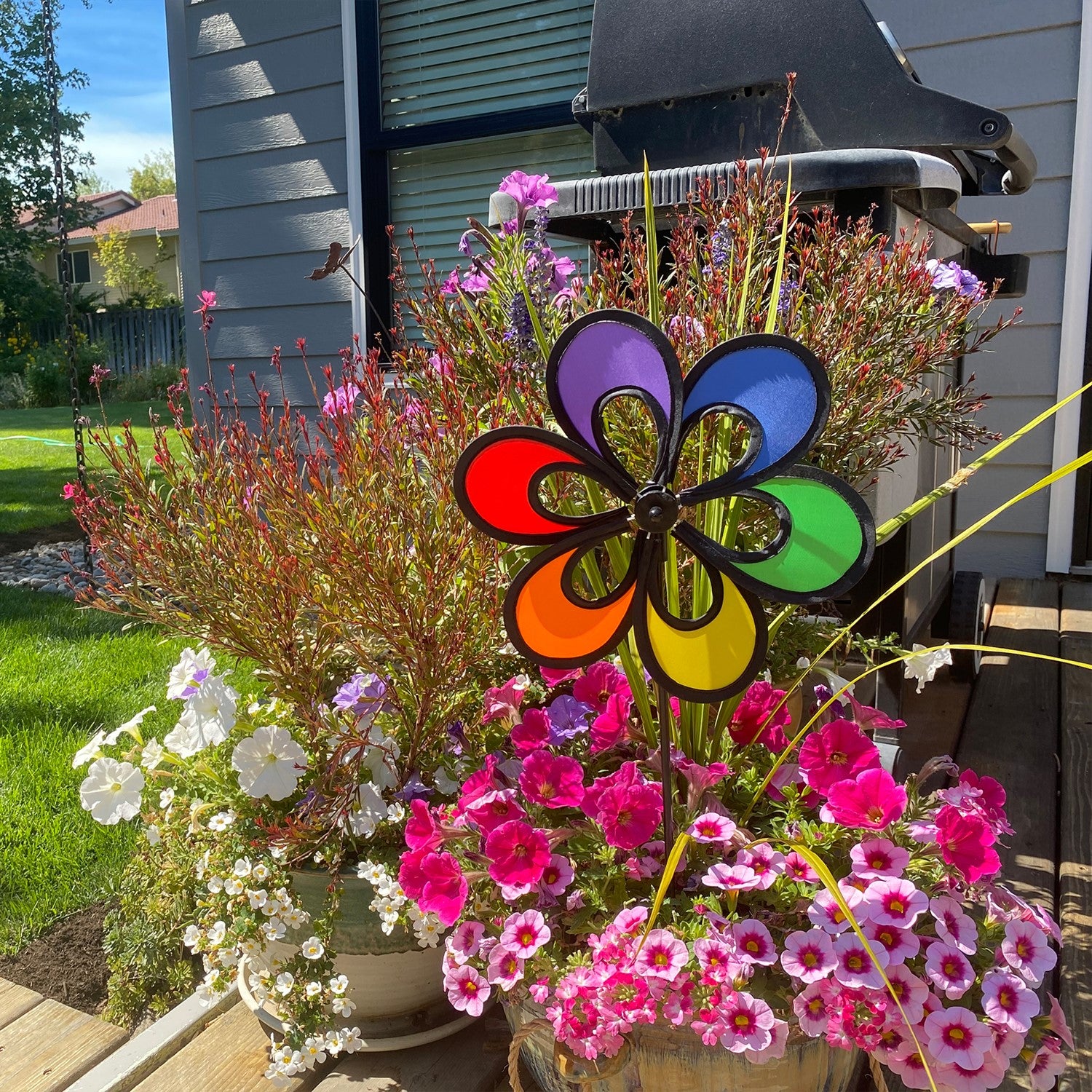 10-inch Rainbow Windee Wheelz Spinner with open-center petal design, spinning in the breeze among flowers in a garden setting.