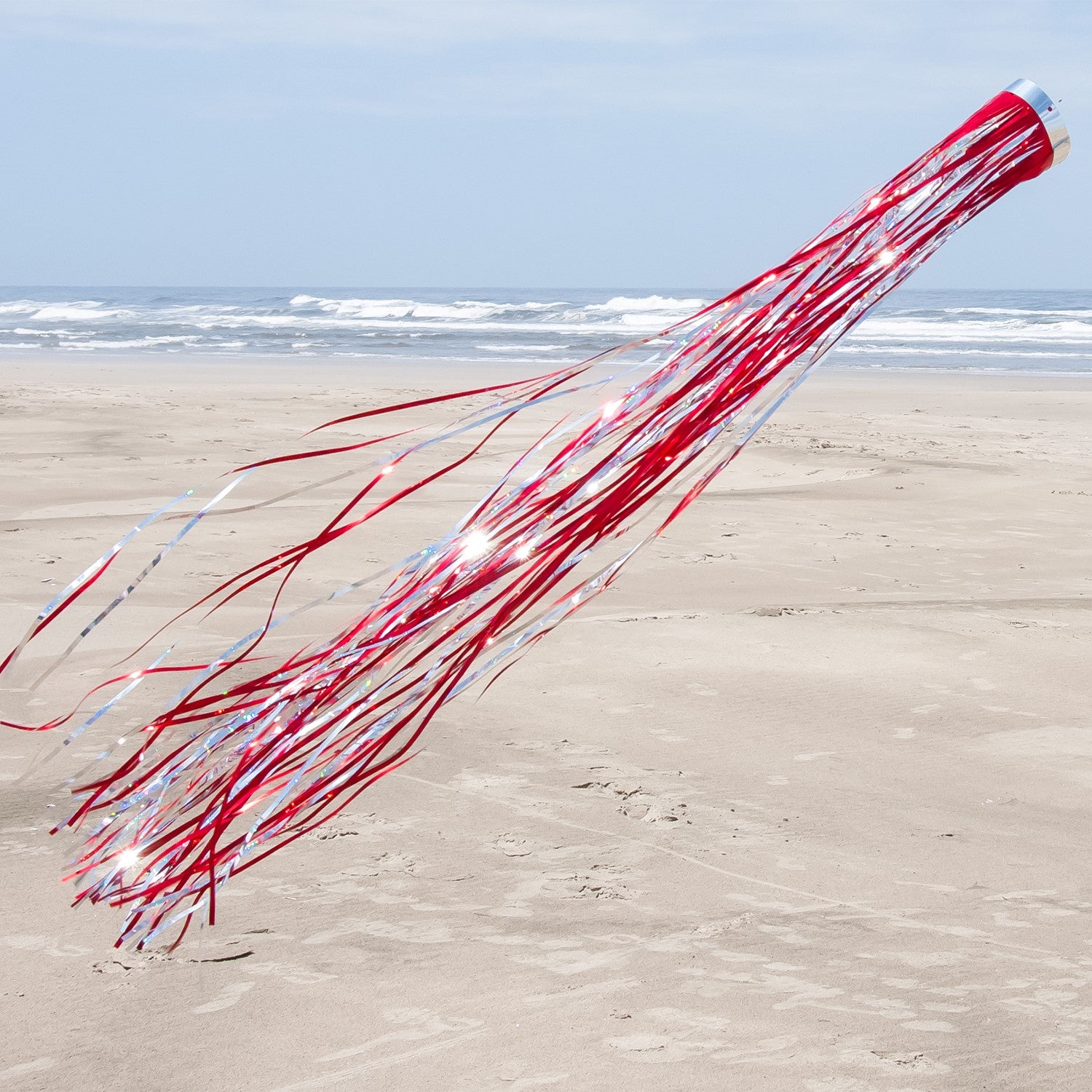 Red 51 Mylar windsock fluttering in the sunlight, showcasing its holographic design and vibrant color in an outdoor garden setting.