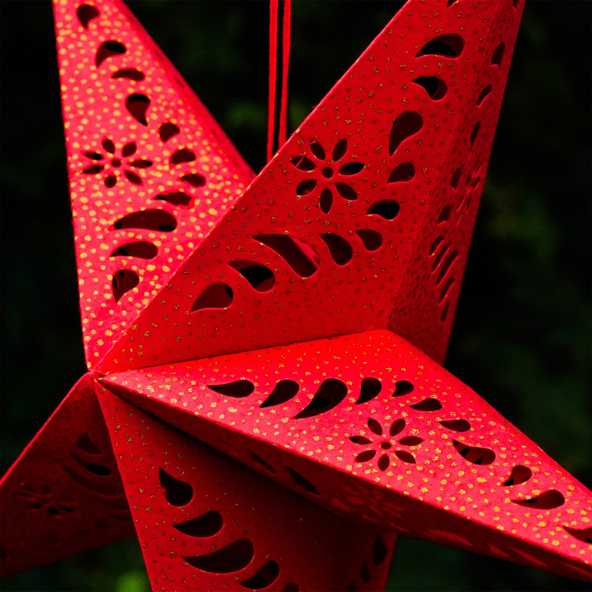 A Red Paper Star Lantern with intricate cutouts, elegantly hanging and illuminated, showcasing its vibrant color and gold accents in warm light.