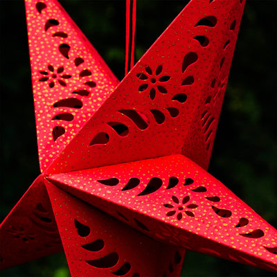 A Red Paper Star Lantern with intricate cutouts, elegantly hanging and illuminated, showcasing its vibrant color and gold accents in warm light.