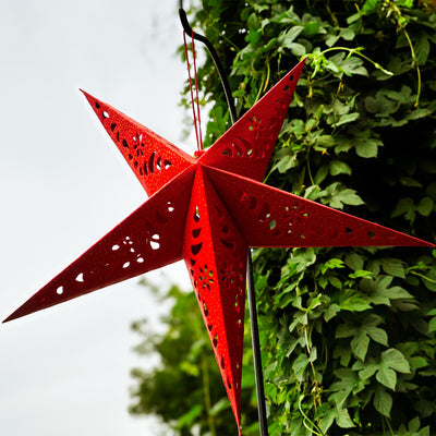 A Red Paper Star Lantern with intricate cutouts, elegantly hanging and illuminated, showcasing its vibrant color and gold accents in warm light.