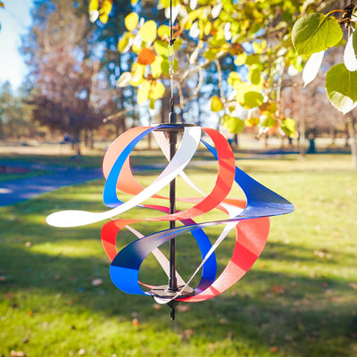 Red, White and Blue Poly Vortex Spinner with interconnected spirals in motion, hanging outdoors amidst greenery, showcasing vibrant colors and patriotic spirit.