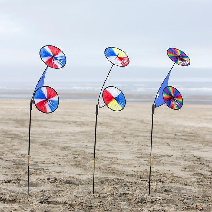 Red, Yellow, Blue & White Space Flower Ground Spinner in motion, featuring two colorful wheels on a sturdy pole in a garden setting.