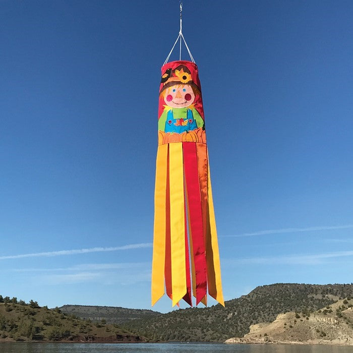 Scarecrow 40" Windsock displayed outdoors, featuring vibrant autumn colors and delightful scarecrow design with fluttering tails in a garden setting.