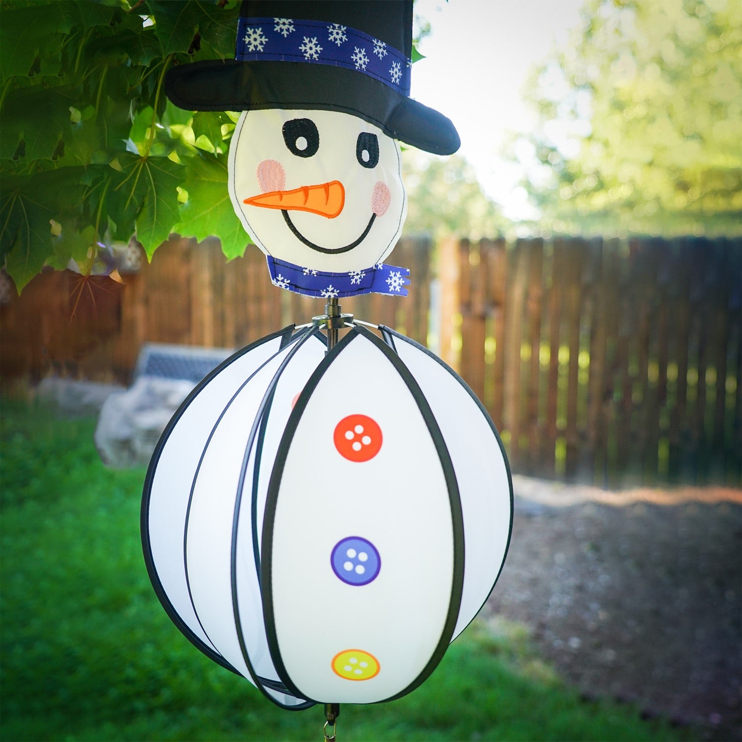 Snowman with Hat Hanging Ball Spinner in a garden setting, showcasing colorful panels and a cheerful, embroidered face, perfect for winter decoration.