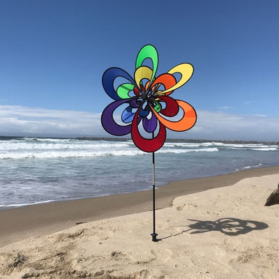 Spectrum Triple Windee Wheelz colorful garden spinner featuring three rotating rainbow flowers, displayed outdoors in a sunny garden setting.