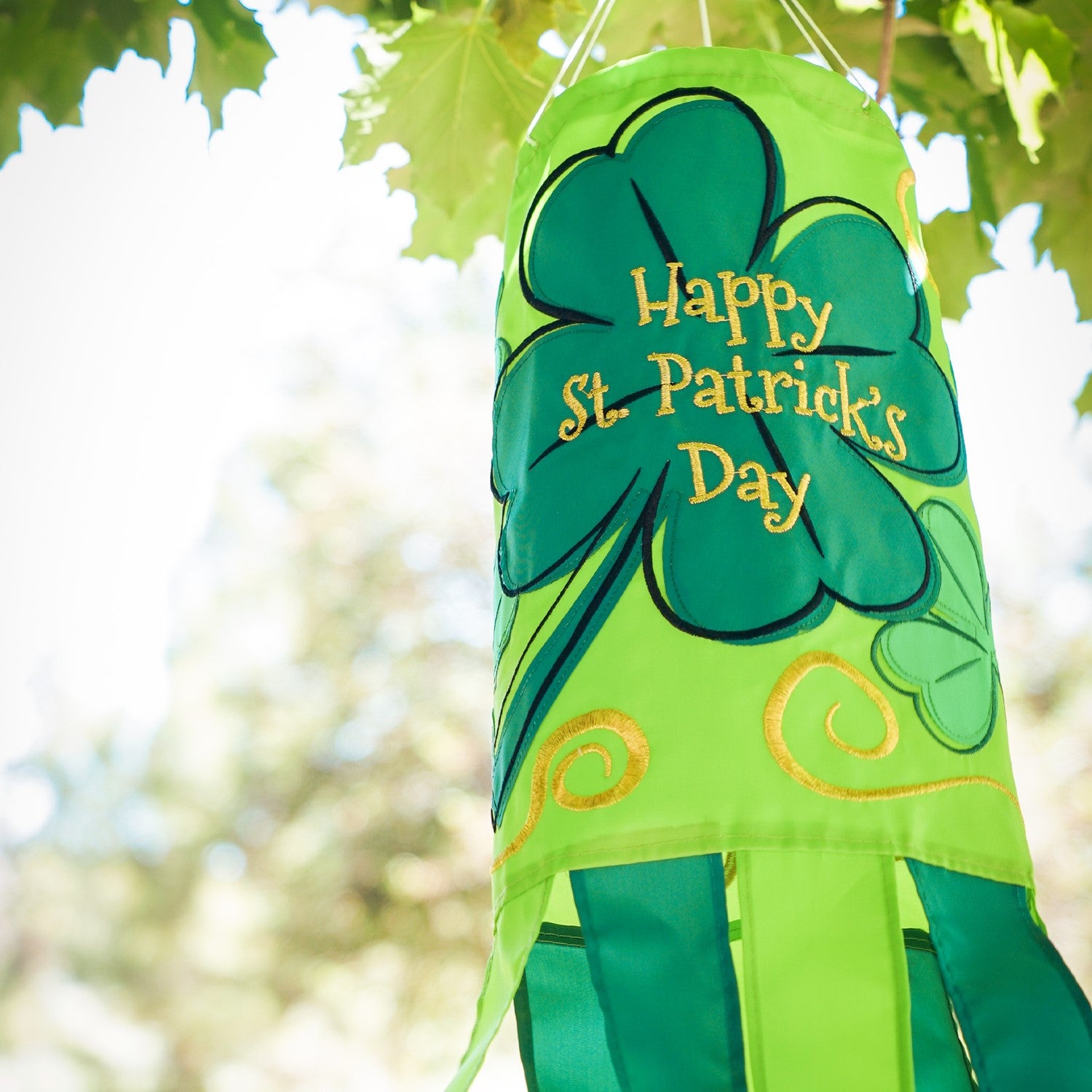 St Patrick's Day 40-inch windsock featuring vibrant four-leaf clover designs and color-coordinated tails, hanging outdoors in a garden.