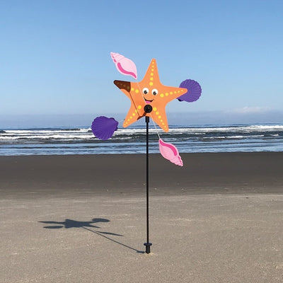 Starfish Whirligig featuring a colorful starfish design spins gracefully in the breeze, set against a vibrant outdoor garden backdrop, enhancing seaside charm.