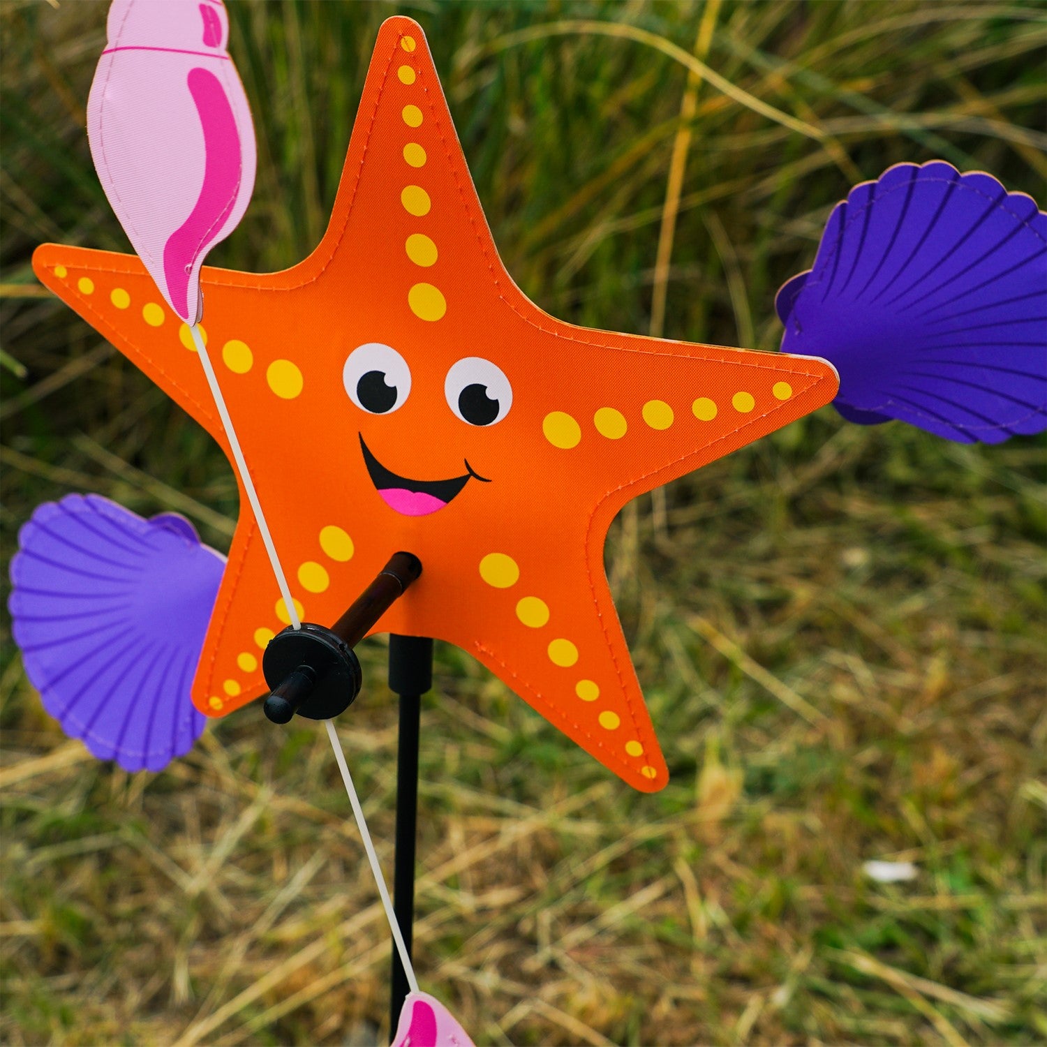 Starfish Whirligig featuring a colorful starfish design spins gracefully in the breeze, set against a vibrant outdoor garden backdrop, enhancing seaside charm.