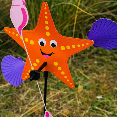 Starfish Whirligig featuring a colorful starfish design spins gracefully in the breeze, set against a vibrant outdoor garden backdrop, enhancing seaside charm.