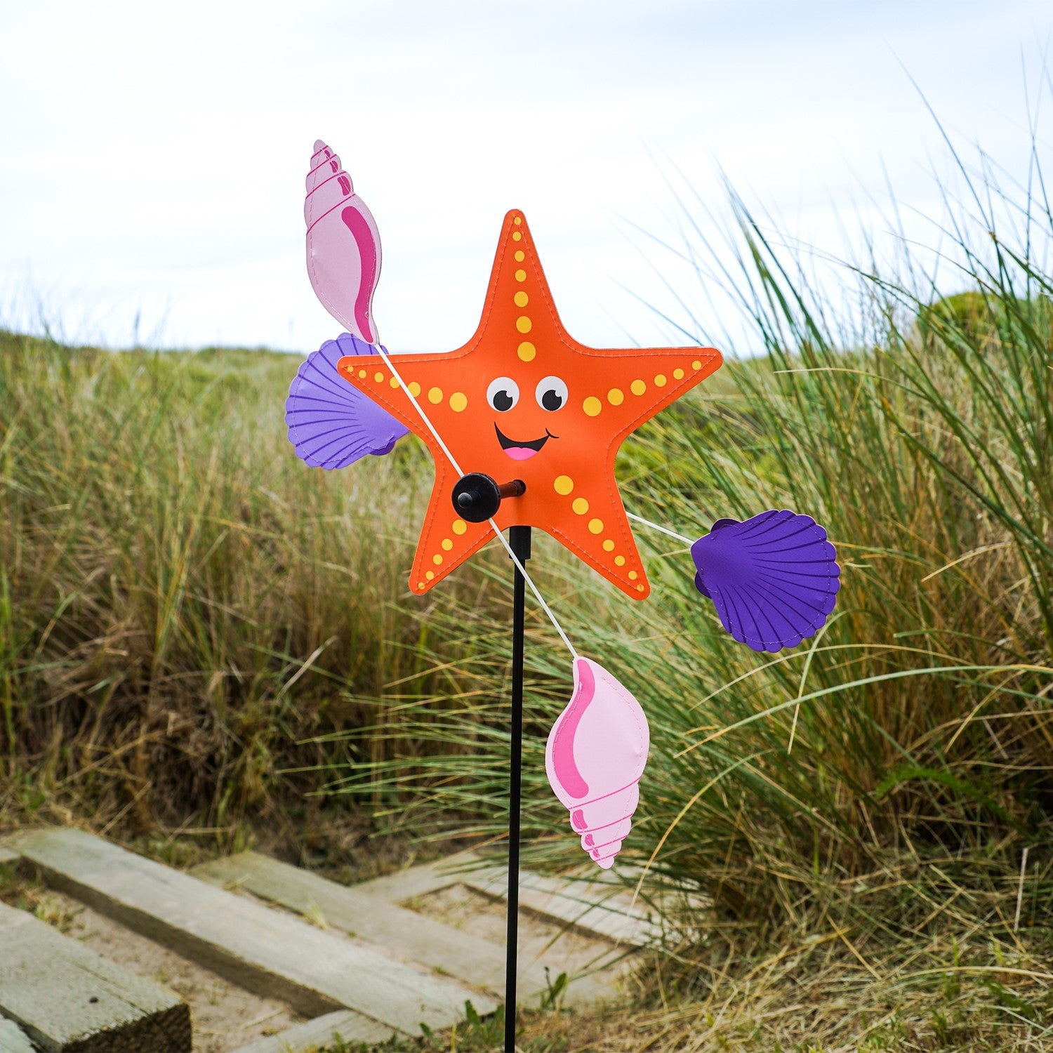 Starfish Whirligig featuring a colorful starfish design spins gracefully in the breeze, set against a vibrant outdoor garden backdrop, enhancing seaside charm.