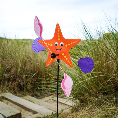 Starfish Whirligig featuring a colorful starfish design spins gracefully in the breeze, set against a vibrant outdoor garden backdrop, enhancing seaside charm.