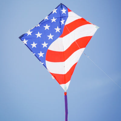 Stars & Stripes 30-inch Diamond Kite with red, white, and blue design, flying high in the sky with decorative tails.