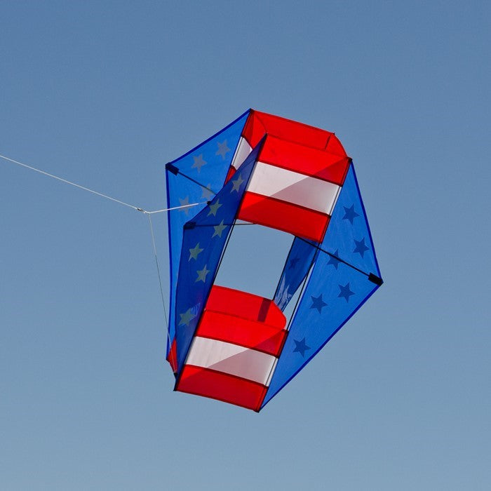 Stars & Stripes Winged Box Kite with a vibrant red, white and blue design soaring against a clear blue sky during an outdoor event.