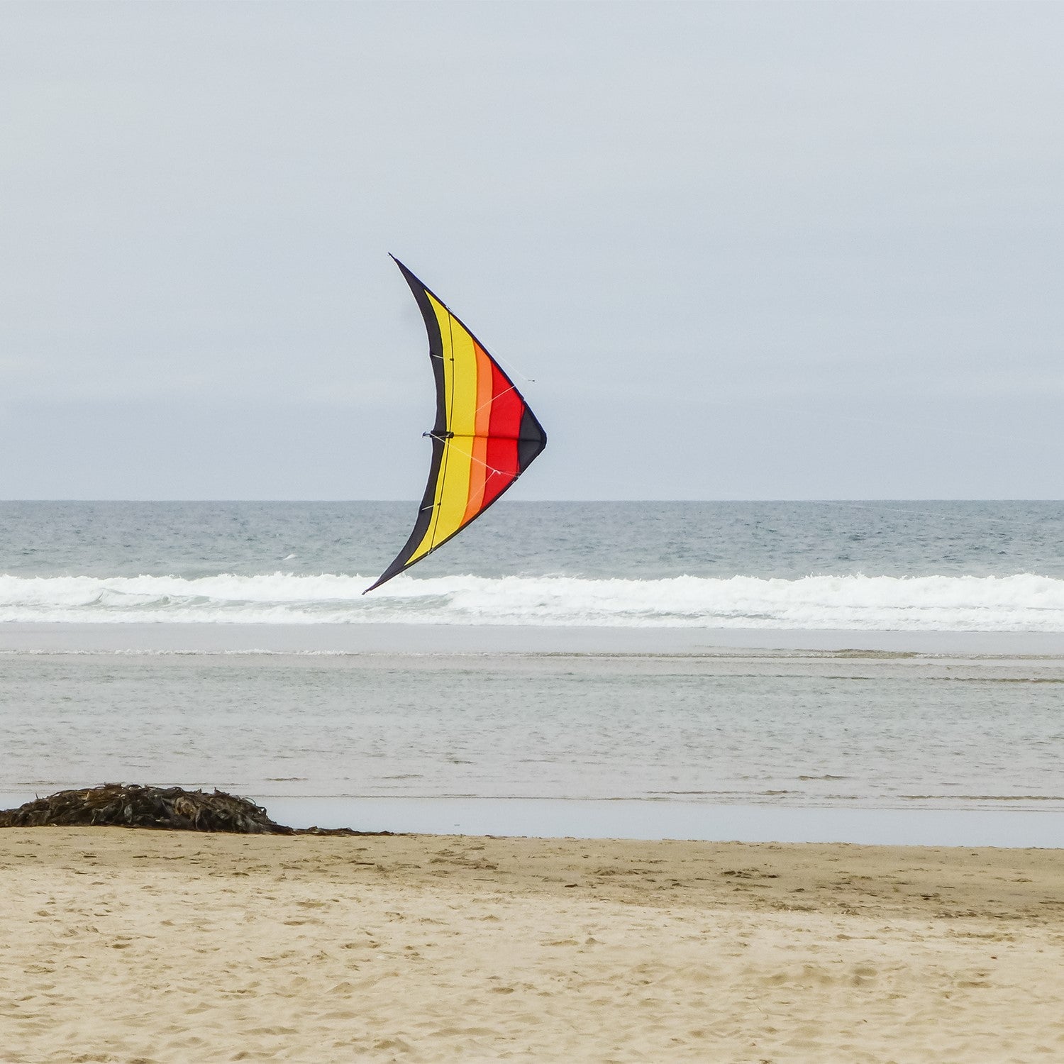 The Sunset 55" Sport Kite showcasing a bold, colorful design in flight against a clear blue sky is perfect for outdoor activities and easily recognizable.