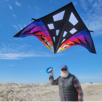 Sweet 16 Delta Kite - Sunset Check, featuring vibrant colors and a large design, soaring high against an open blue sky during outdoor flight.
