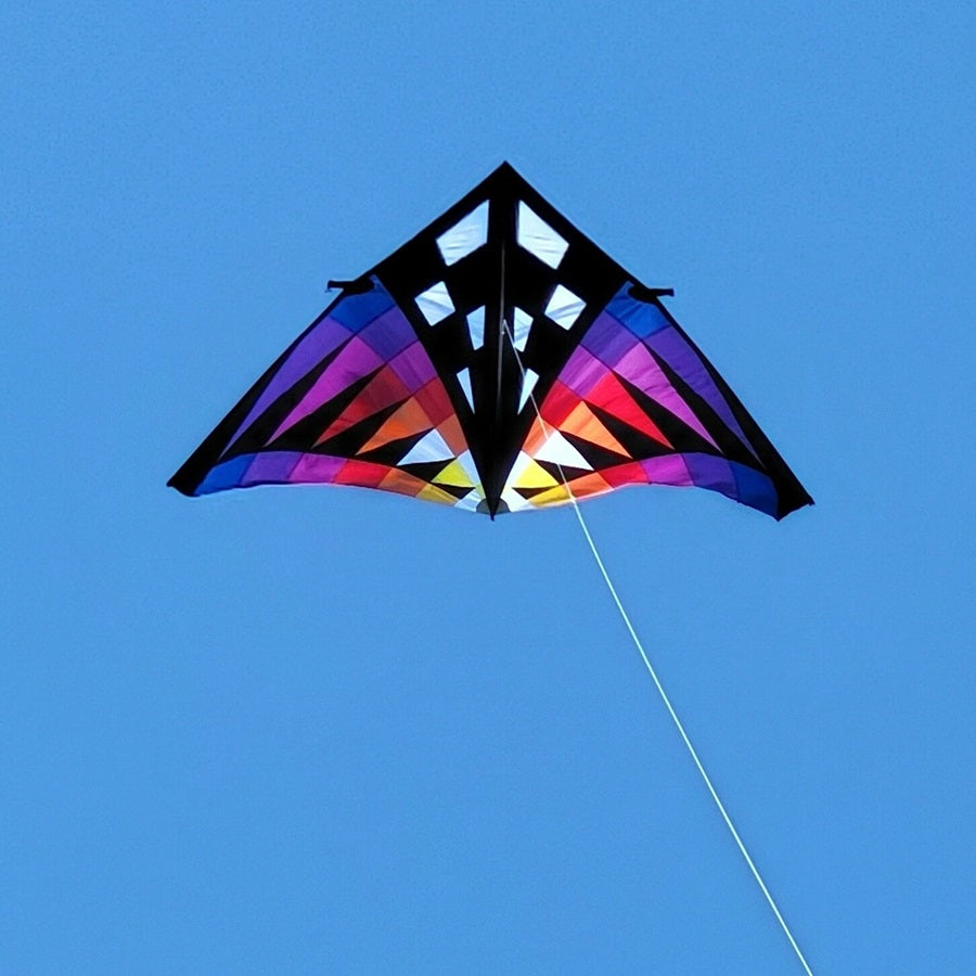 Sweet 16 Delta Kite - Sunset Check, featuring vibrant colors and a large design, soaring high against an open blue sky during outdoor flight.