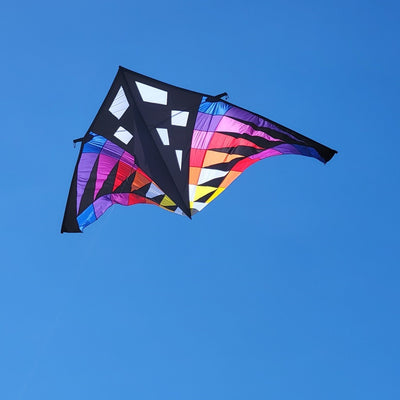 Sweet 16 Delta Kite - Sunset Check, featuring vibrant colors and a large design, soaring high against an open blue sky during outdoor flight.