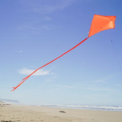 Tangerine Colorfly 30-inch diamond kite soaring against a blue sky, featuring three colorful tails and a lightweight design for easy flying.