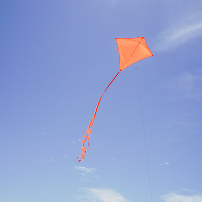 Tangerine Colorfly 30-inch diamond kite soaring against a blue sky, featuring three colorful tails and a lightweight design for easy flying.
