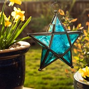 Teal 5-Point Star Hanging Tealight Lantern with textured glass panels and metal accents, suspended outdoors against a scenic backdrop.