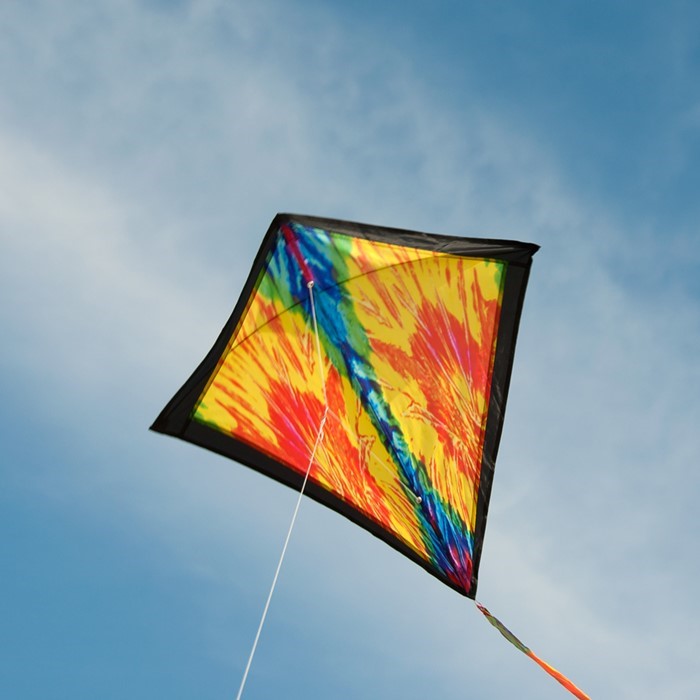 Tie Dye 30 inch Diamond Kite flying high in the sky with vibrant colors and 12-foot streamer tails swaying in the wind.
