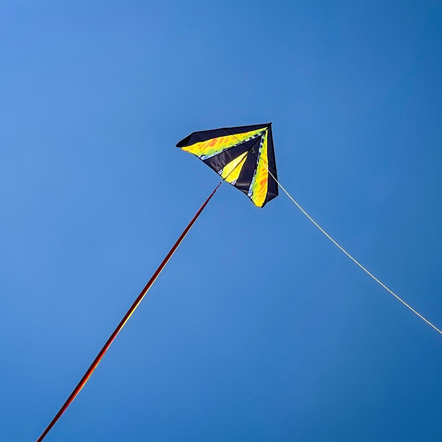 Tie Dye 46" Delta Kite soaring against a blue sky, featuring colorful streamer tails and tie-dye pattern, ideal for outdoor fun.