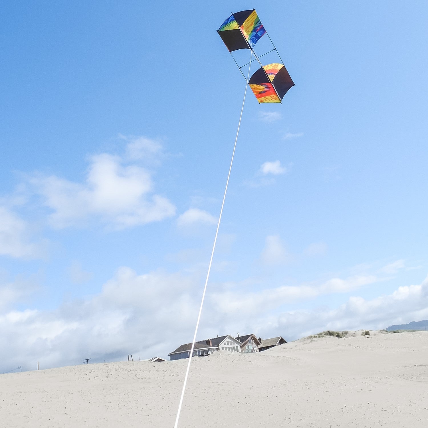 Tie Dye Box Kite flying high against a blue sky, showcasing its vibrant tie-dye design and sturdy fiberglass structure.