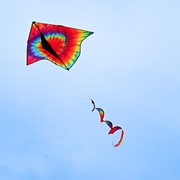 Tie Dye Delta Kite with Spinning Tail flying in the sky, showcasing its vibrant colors and unique design against a clear blue backdrop.