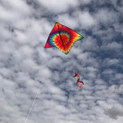 Tie Dye Delta Kite with Spinning Tail flying in the sky, showcasing its vibrant colors and unique design against a clear blue backdrop.