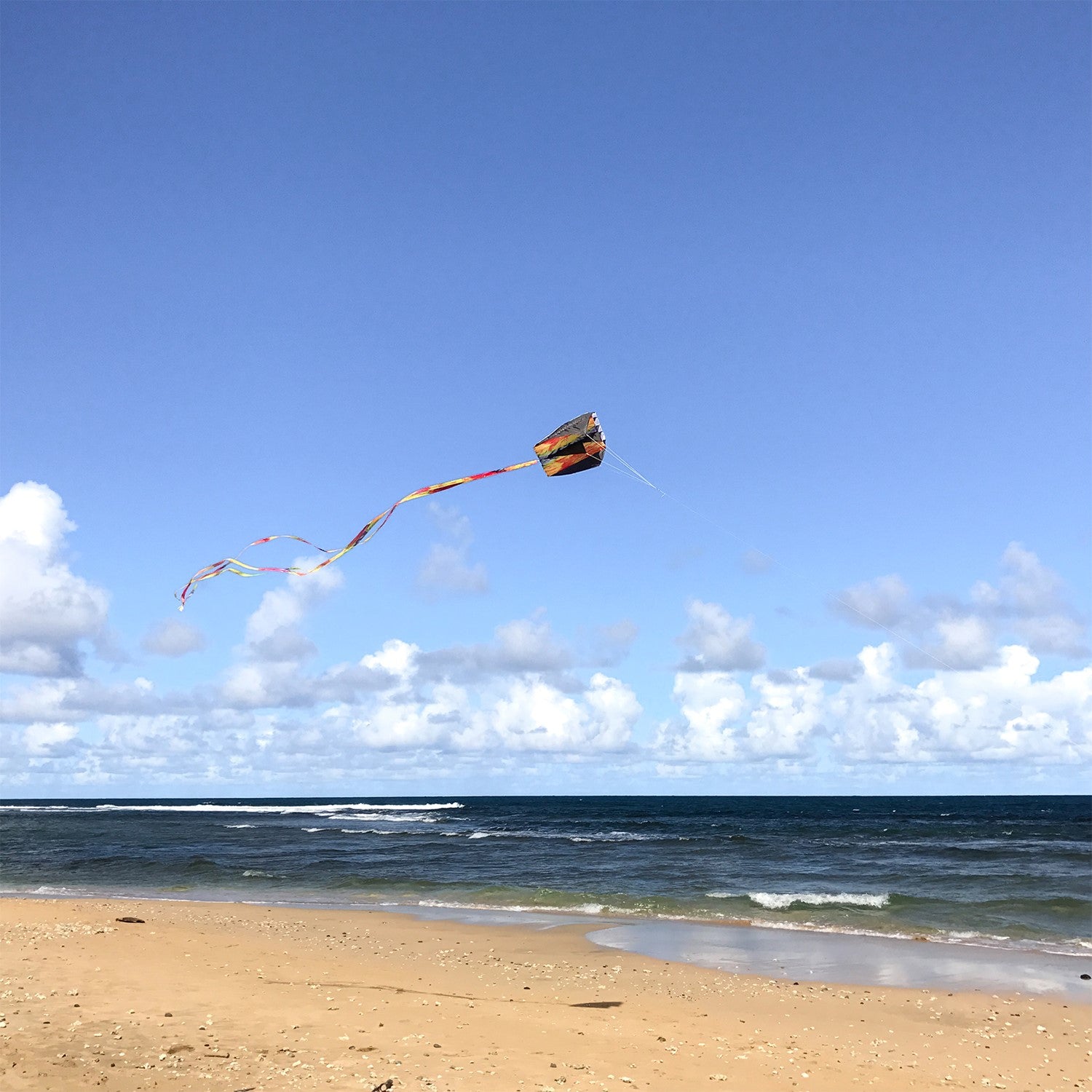 Tie Dye Pouch Parafoil Kite soaring in the blue sky, featuring a colorful design and three coordinating kite tails.