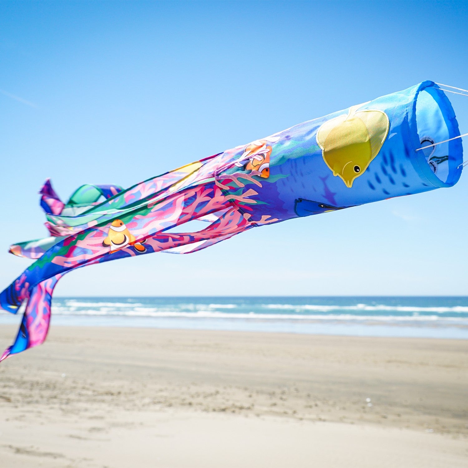 Tropical Fish 40\" Illusion Windsock displaying a vivid fish design and colorful tails, fluttering in a gentle breeze in a garden setting.