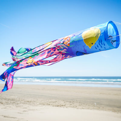 Tropical Fish 40\" Illusion Windsock displaying a vivid fish design and colorful tails, fluttering in a gentle breeze in a garden setting.