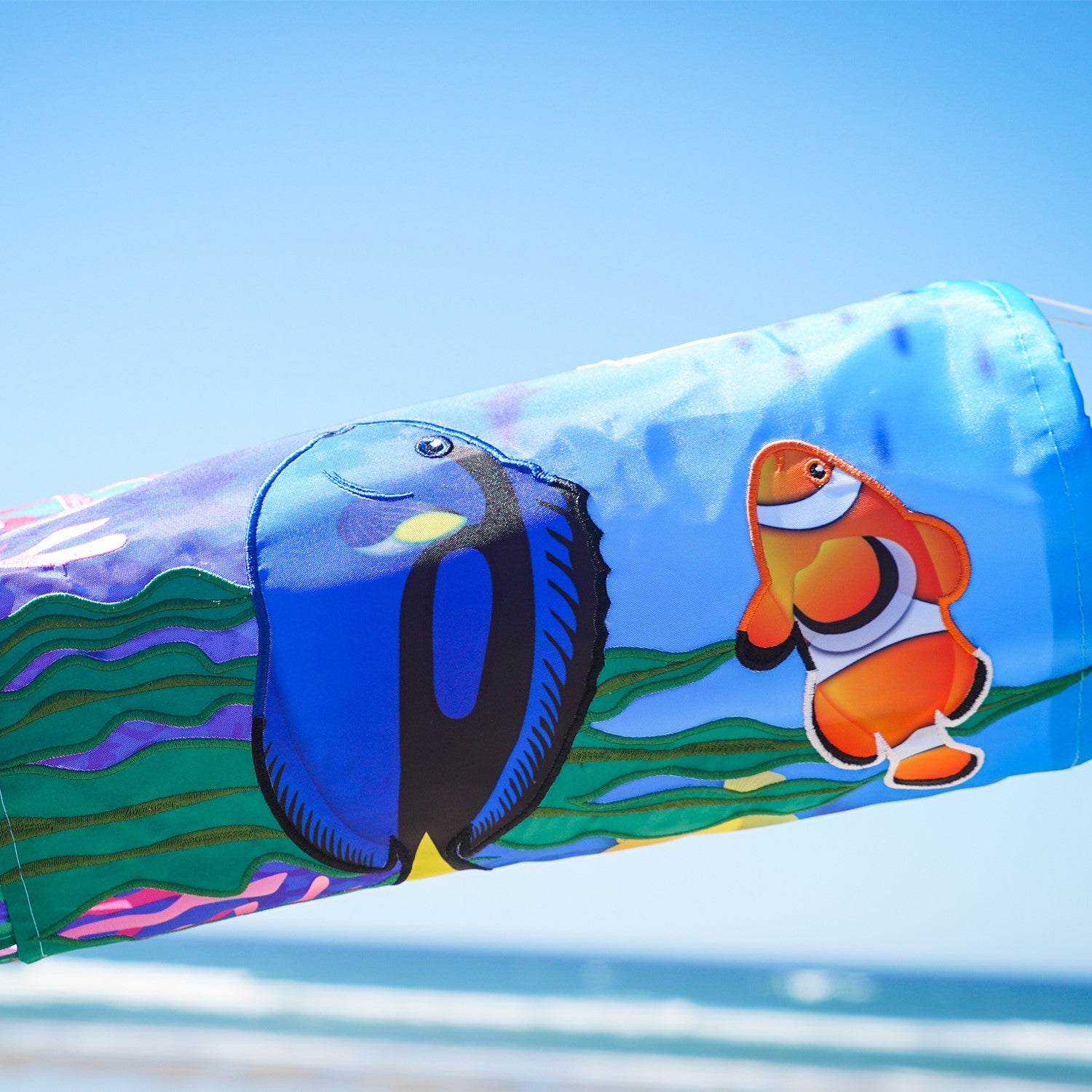 Tropical Fish 40\" Illusion Windsock displaying a vivid fish design and colorful tails, fluttering in a gentle breeze in a garden setting.