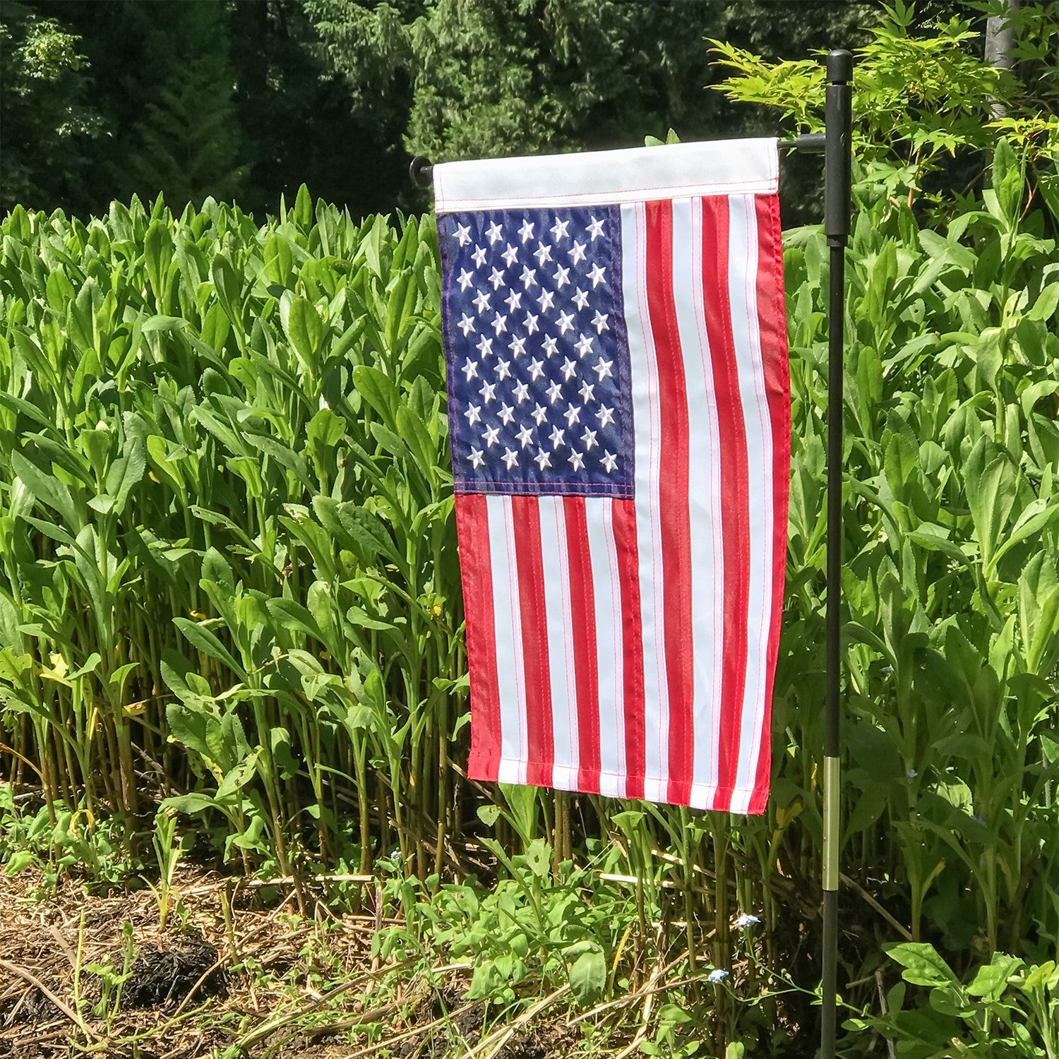 US Flag Embroidered Garden Flag with embroidered stars displayed on a flagpole in a vibrant garden setting.