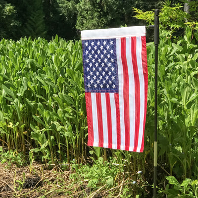 US Flag Embroidered Garden Flag with embroidered stars displayed on a flagpole in a vibrant garden setting.