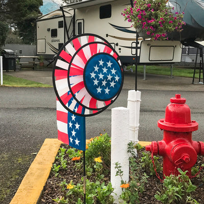 USA Flag Dual Spinner Wheels with red, white and blue design in a garden setting, featuring a garden flag and a robust pole for display.