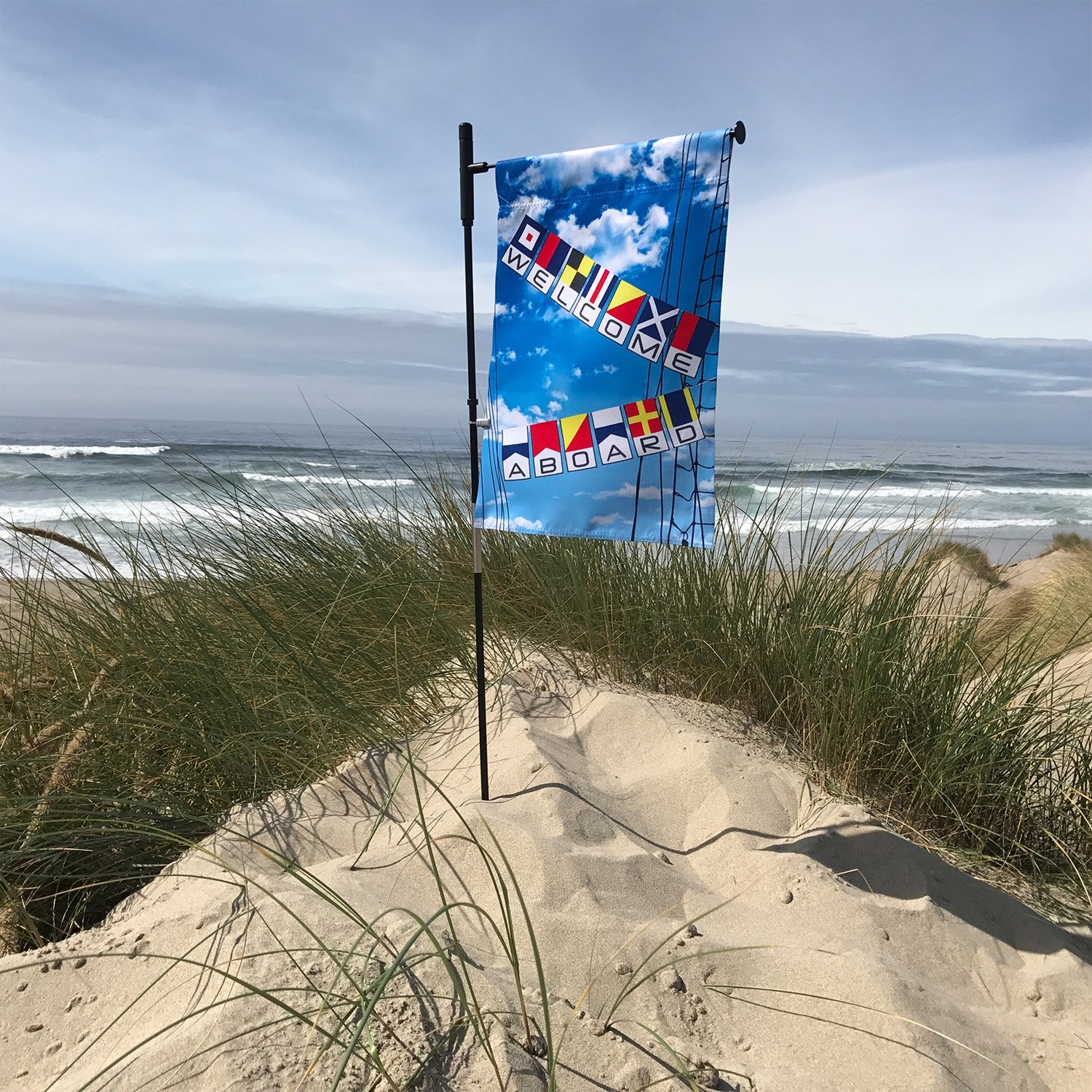 Welcome Aboard Lustre Garden Flag featuring a nautical design, displayed on a garden flag stand in a sunny outdoor setting.