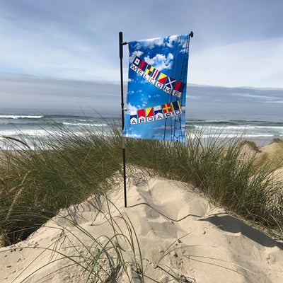 Welcome Aboard Lustre Garden Flag featuring a nautical design, displayed on a garden flag stand in a sunny outdoor setting.