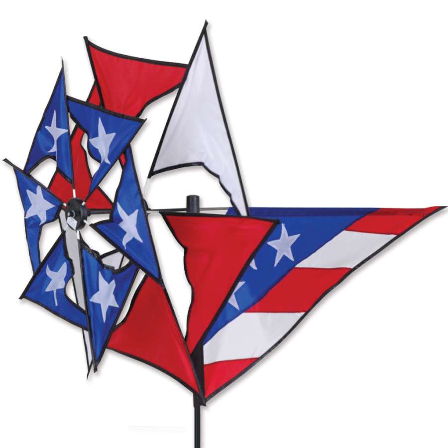 Windmill Spinner in vivid red, white, and blue, spinning gracefully in a lush garden against a clear blue sky.