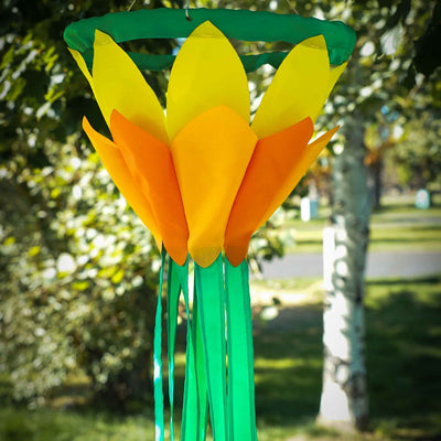 Colorful Yellow 38-Inch Lotus Flower Windsock featuring vibrant yellow and orange petals with green tails, displayed outdoors in a garden setting.